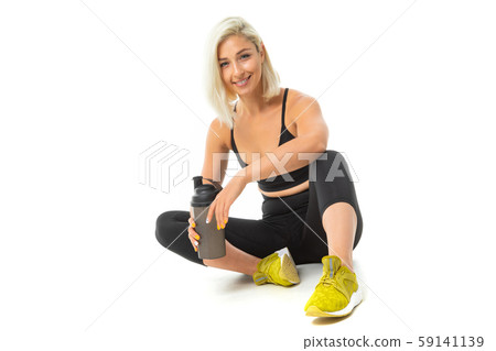 Sport caucasian girl sits on a floor in sport wear and keep a bottle with water in her hands Sport caucasian girl sits on a floor in sport wear and keep a bottle with water in her hands 59141139