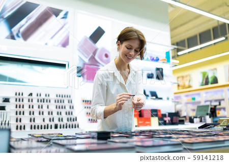 Young smiling woman in cosmetics shop is testing eye-shadows with aplicator Young smiling woman in cosmetics shop is testing eye-shadows with aplicator 59141218