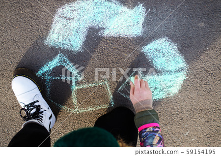 A teenager draws a symbol of ecology with chalk on asphalt. Chalk is green. A teenager draws a symbol of ecology with chalk on asphalt. Chalk is green. 59154195