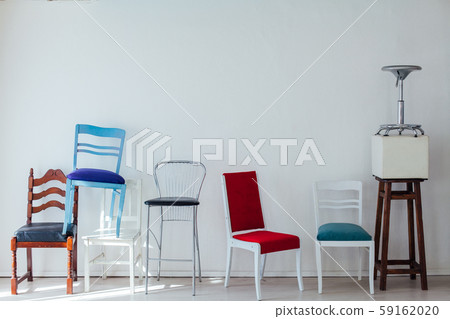 many different chairs of different colors stand at the white wall 59162020