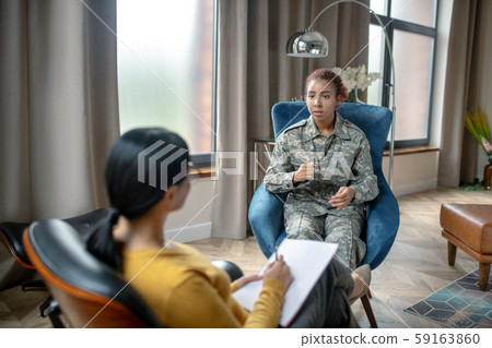 Young military woman sharing her thoughts with psychoanalyst Young military woman sharing her thoughts with psychoanalyst 59163860