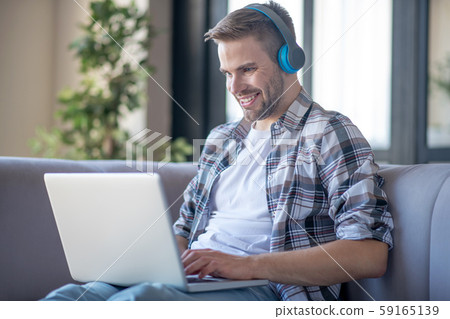 Cheerful man wearing headphones watching movie on laptop 59165139