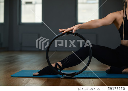 Young, beautiful, athletic girl is doing exercises with the Pilates ring in the gym on a gray 59177250