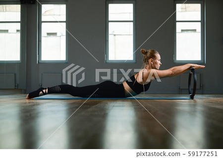 Young, beautiful, athletic girl is doing exercises with the Pilates ring in the gym on a gray 59177251