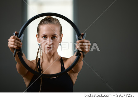 Young, beautiful, athletic girl is doing exercises with the Pilates ring in the gym on a gray 59177253
