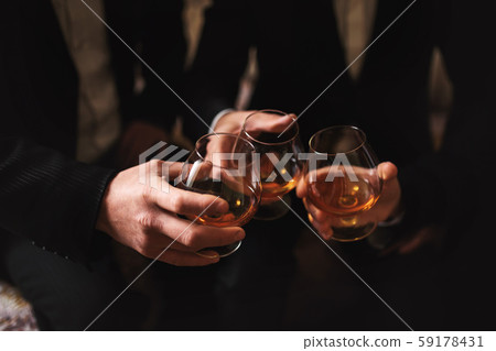 Business meeting. Men hold glasses of whiskey. Men's Party. Hand with a drink of alcohol Business meeting. Men hold glasses of whiskey. Men's Party. Hand with a drink of alcohol 59178431