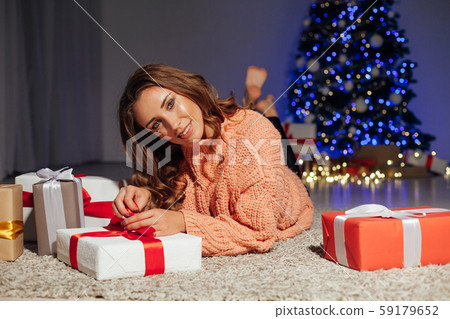 Beautiful woman opens gifts at the Christmas tree at night at home New Year lights garlands Beautiful woman opens gifts at the Christmas tree at night at home New Year lights garlands 59179652