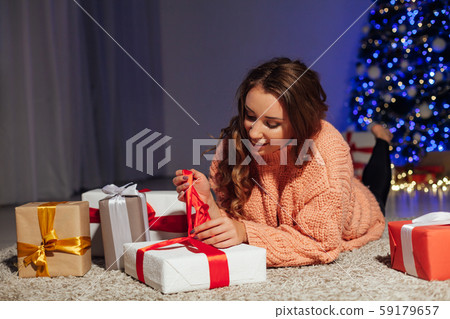 Beautiful woman opens gifts at the Christmas tree at night at home New Year lights garlands Beautiful woman opens gifts at the Christmas tree at night at home New Year lights garlands 59179657