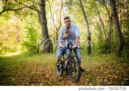 Excited father and his son having fun together at the green park, teaching son how to ride a bicycle 59182716