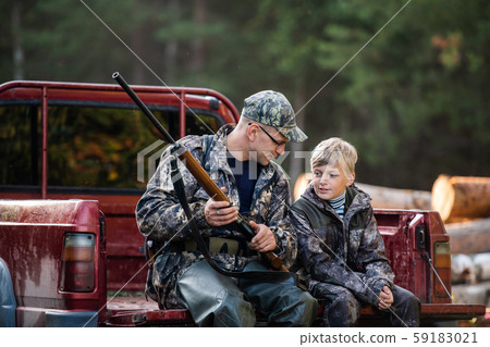 Man at his truck with his son in the forest. Hunter teaches young boy how to use shotgun rifle. Man at his truck with his son in the forest. Hunter teaches young boy how to use shotgun rifle. 59183021