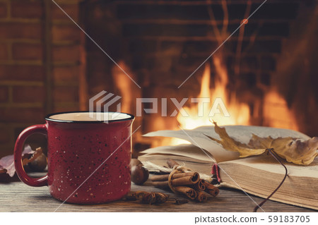 Red mug with hot tea and an open book in front of a burning fireplace, comfort, relaxation and Red mug with hot tea and an open book in front of a burning fireplace, comfort, relaxation and 59183705