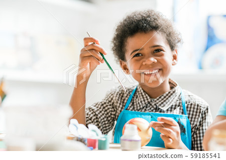 Cheerful schoolboy with paintbrush making Christmas toy ball at lesson Cheerful schoolboy with paintbrush making Christmas toy ball at lesson 59185541