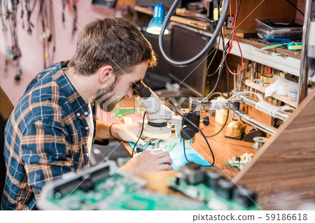 Professional gadget repairman looking in microscope while trying to find problem 59186618