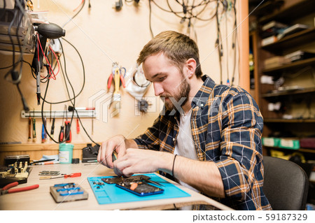 Professional repairman bending over broken smartphone and fixing tiny details 59187329