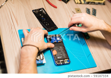 Hands of repairman over broken gadget using tweezers to fix tiny parts or bolts 59187334