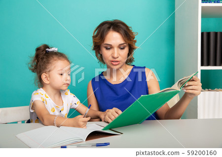 Daughter with mother sitting at the table together and doing homework. 59200160