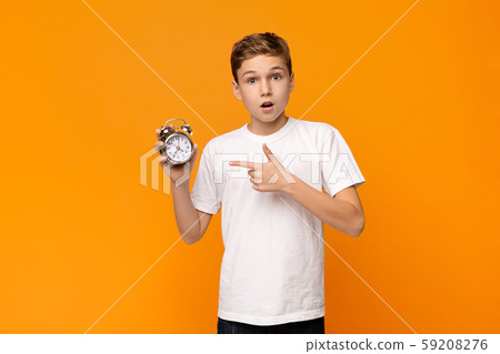 Astonished teenage boy pointing at alarm clock Astonished teenage boy pointing at alarm clock 59208276