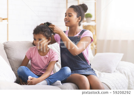 Caring african teenage girl brushing her little sister hair at home Caring african teenage girl brushing her little sister hair at home 59208292