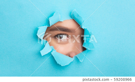 Woman looking at camera through torn blue paper 59208966