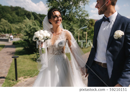 Beautiful bride with her handsome groom walking outside on theri wedding day. Happy newlyweds Beautiful bride with her handsome groom walking outside on theri wedding day. Happy newlyweds 59210151