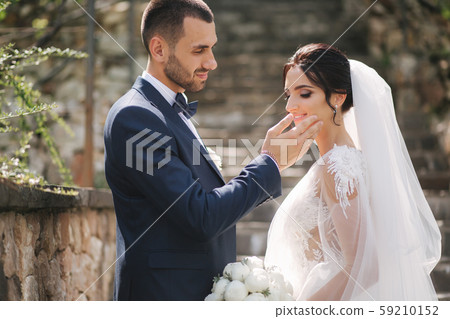 Beautiful bride with her handsome groom walking outside on theri wedding day. Happy newlyweds 59210152