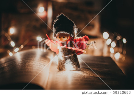 wooden angel christmas garland stands on a book, in the background is an LED garland. Christmas wooden angel christmas garland stands on a book, in the background is an LED garland. Christmas 59210693