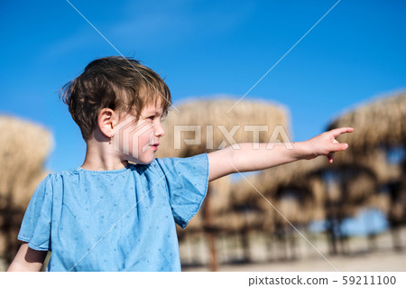 A small girl standing among straw parasols outdoors on beach. 59211100