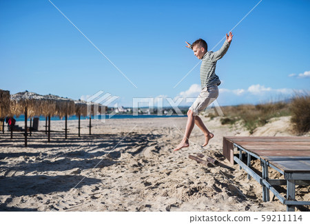 A small boy playing outdoors on sand beach, jumping. 59211114