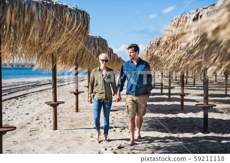 Young couple walking outdoors on beach, holding hands. Copy space. 59211118