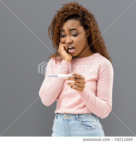 Portrait of scared young woman holding positive pregnancy test 59211884