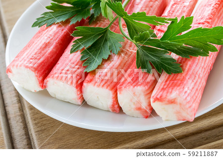 Row of surimi crab sticks and parsley on a white saucer over a brown wooden cutting board. Row of surimi crab sticks and parsley on a white saucer over a brown wooden cutting board. 59211887