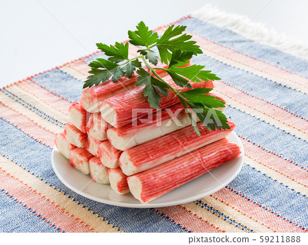 Heap of surimi crab sticks and parsley on a white saucer over a striped table mat. Heap of surimi crab sticks and parsley on a white saucer over a striped table mat. 59211888