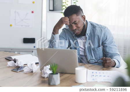 Stressed african worker looking to laptop screen with despair Stressed african worker looking to laptop screen with despair 59211896