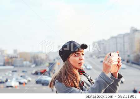 girl taking pictures on a phone on a city street 59211905