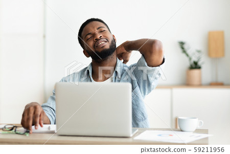 Black man suffering from neck pain while working on laptop Black man suffering from neck pain while working on laptop 59211956