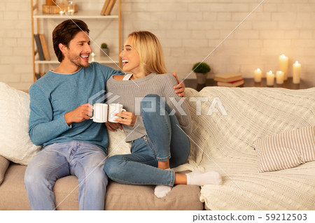 Loving Couple Clanging Cups Together Sitting On Couch At Home Loving Couple Clanging Cups Together Sitting On Couch At Home 59212503