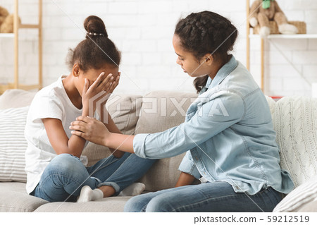 Young crying girl being consoled by her elder sister 59212519