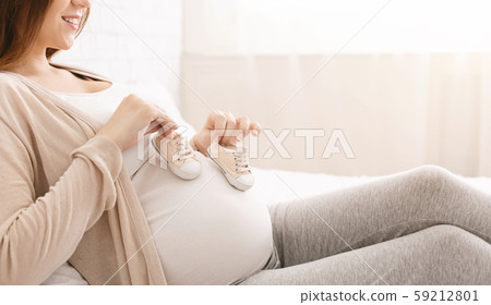 Pregnant woman playing with tiny shoes, stepping on belly 59212801