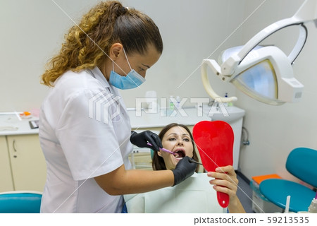 Woman patient looking in the mirror at the teeth, sitting in the dental chair 59213535
