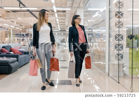 Two adult women with shopping bags walking in mall, women smiling and looking at showcase 59213725