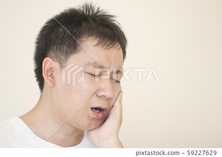 Indoor shot of young male feeling pain, holding his cheek with hand, suffering from bad toothache.Concept healthcare and medical. 59227629