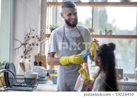 Beaming father taking detergents while cleaning kitchen with daughter Beaming father taking detergents while cleaning kitchen with daughter 59228450
