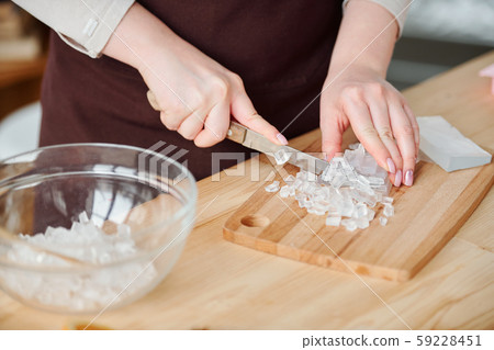 Hands of young craftswoman with knife cutting transparent soap mass on board 59228451