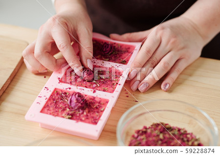 Hands of young woman putting small rosebuds on top of pink soap bars 59228874