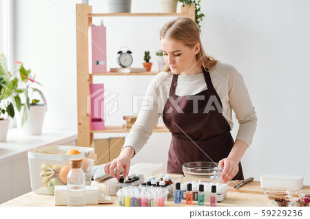 Young blonde craftswoman in apron choosing scent for handmade soap 59229236