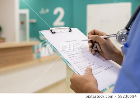 Hands of young mixed-race professional with pen making medical notes in document Hands of young mixed-race professional with pen making medical notes in document 59230584