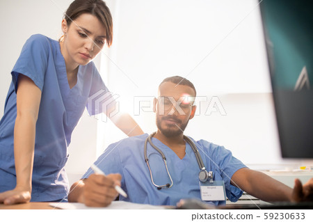 One of young clinicians showing his notes to colleague during discussion 59230633