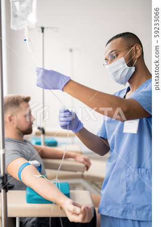 Intern in uniform, protective mask and gloves preparing dropper for patient Intern in uniform, protective mask and gloves preparing dropper for patient 59233066