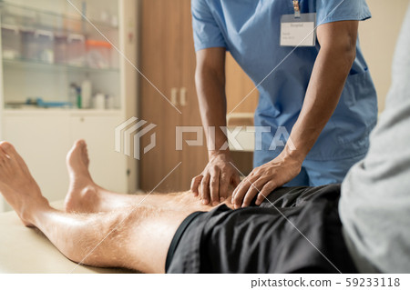 Hands of mixed-race clinician in blue uniform massaging one of legs of patient Hands of mixed-race clinician in blue uniform massaging one of legs of patient 59233118