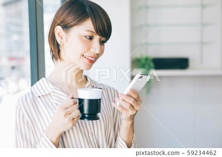 Woman drinking coffee while looking at smartphone during work break 59234462